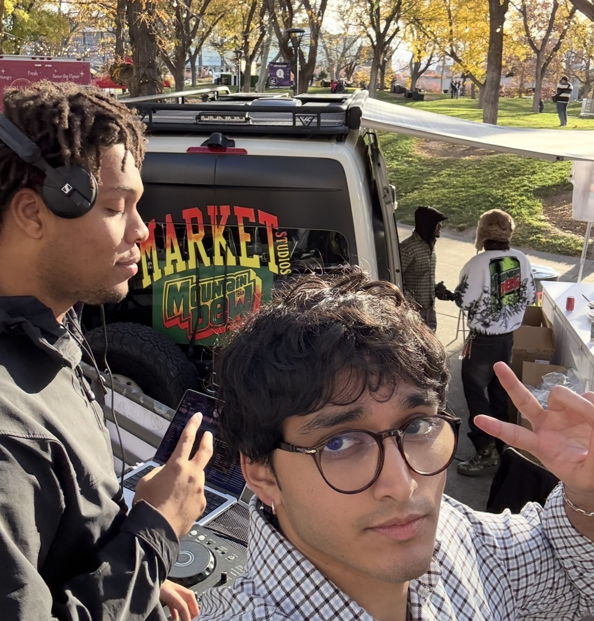 A daytime DJ setup beside a Market and Mountain Dew van
