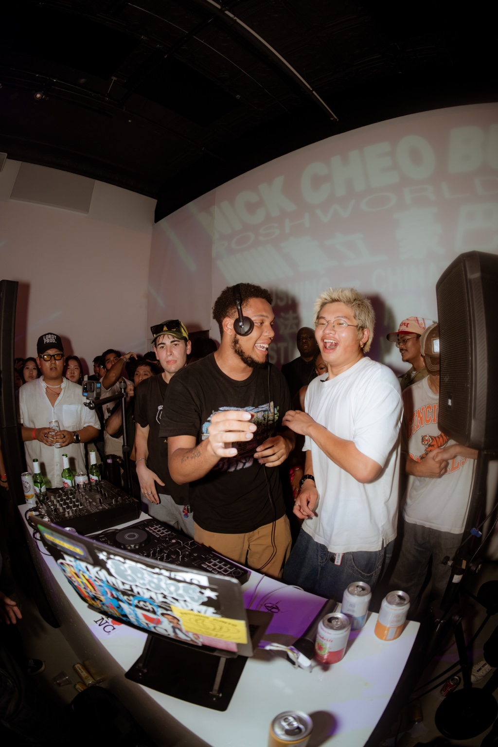 DJs and a crowd beneath a Posh projection